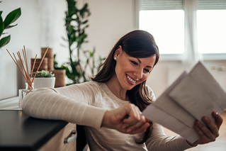 Woman smiling looking at three pieces of mail.